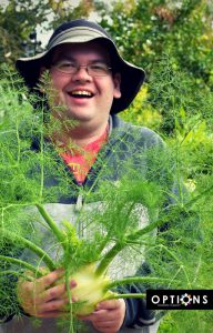man holding fennel in lush Edible Garden