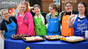 Group of adults wearing colourful aprons selling cakes for Australia's Biggest Morning Tea